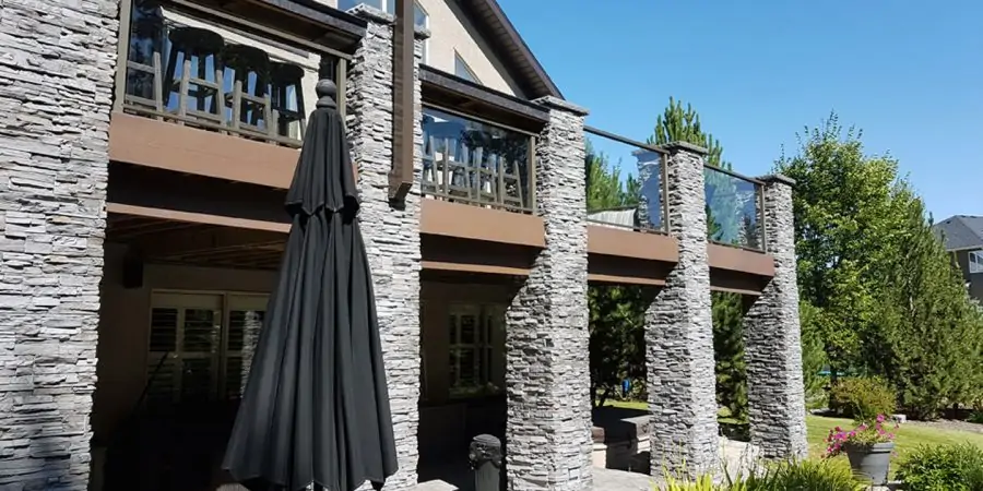 Executive multi-level residential deck featuring stacked stone veneer pillars and clean glass railings in Calgary.